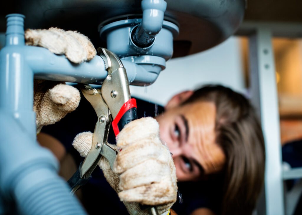 Plumber fixing a pipe under the sink using a wrench tool.